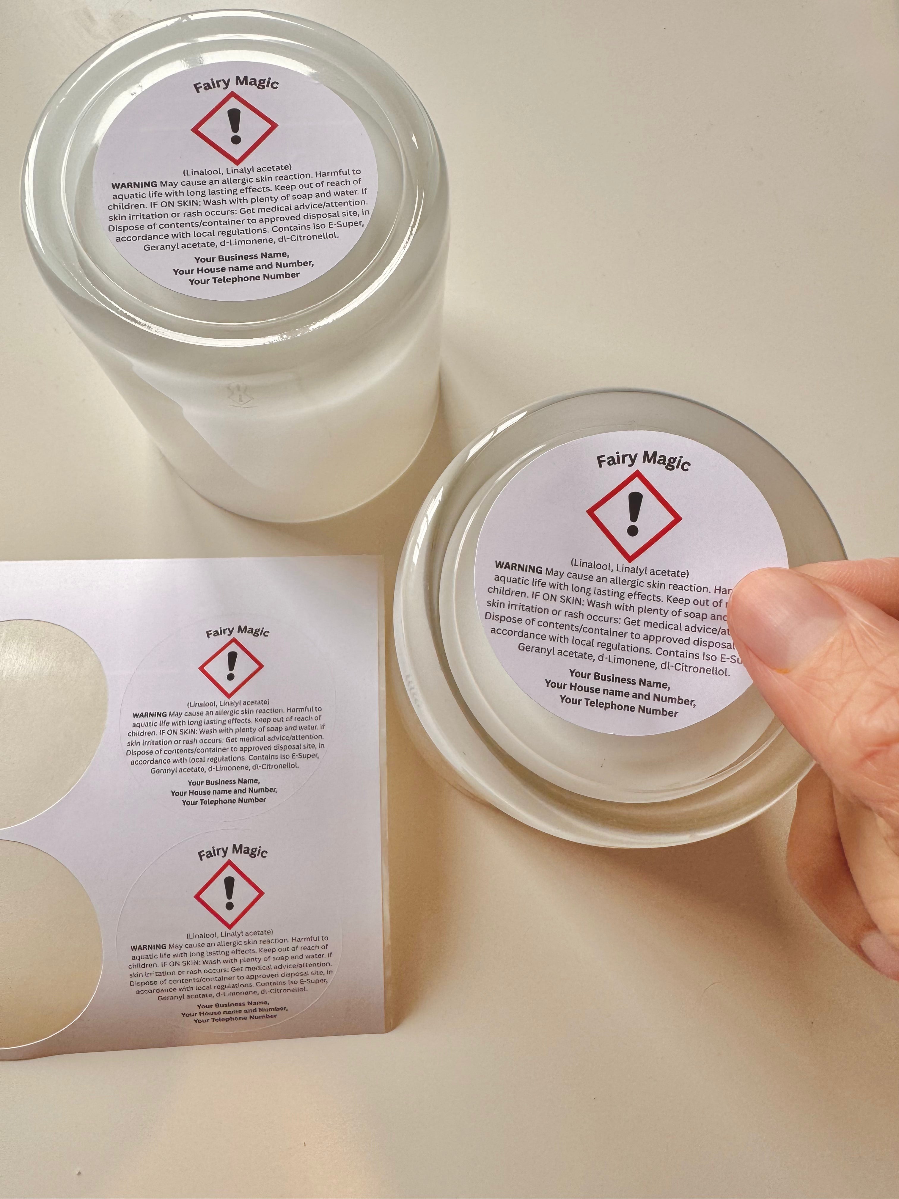 Close-up of a hand holding a candle jar labeled “Fairy Magic” beside matching CLP labels on a beige surface, showing the label application process in warm, natural light.
